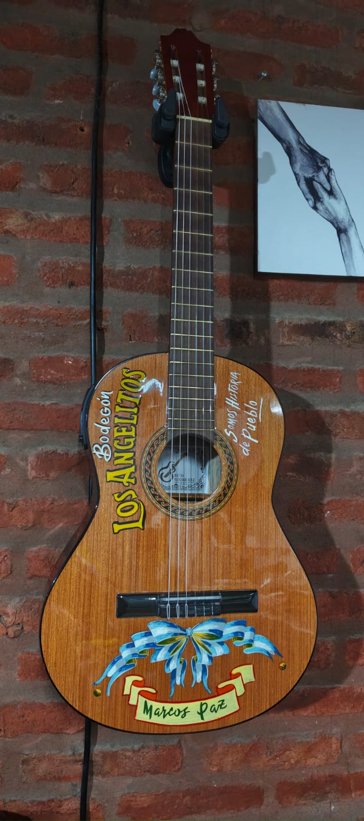 Guitarra criolla restaurada y pintada a mano colgada en la pared del taller